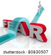 stock photo : A man jumps over the word fear on an arrow, illustrating the bravery and courage needed to overcome and conquer one's fears and anxieties